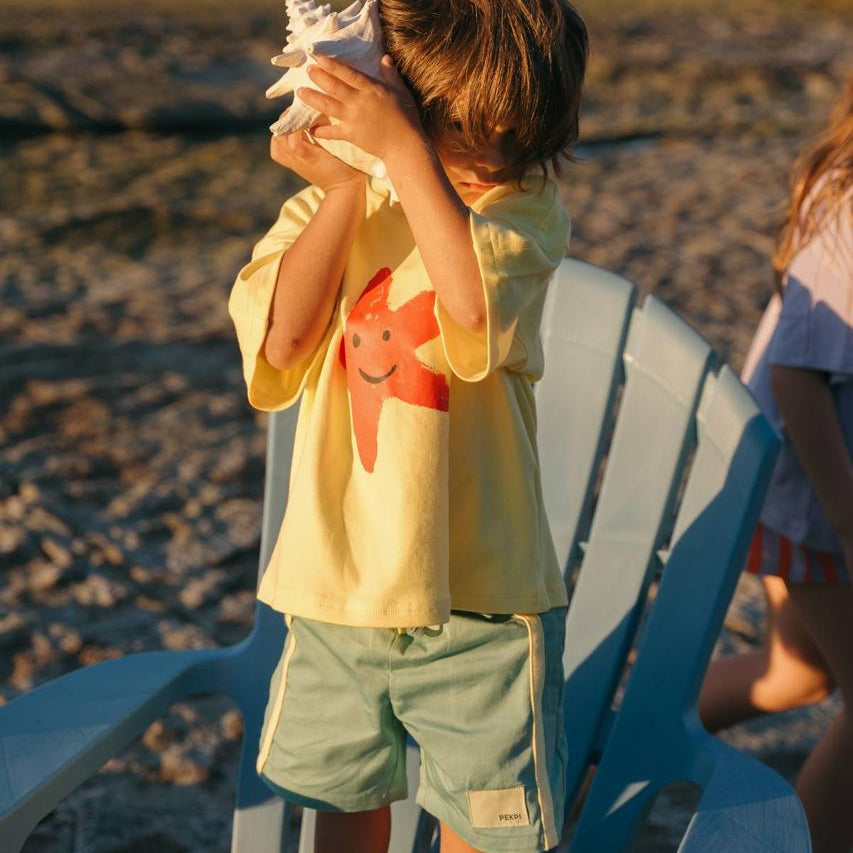 Green Reef Shorts - boy listening to shell with Starfish Tee Yellow