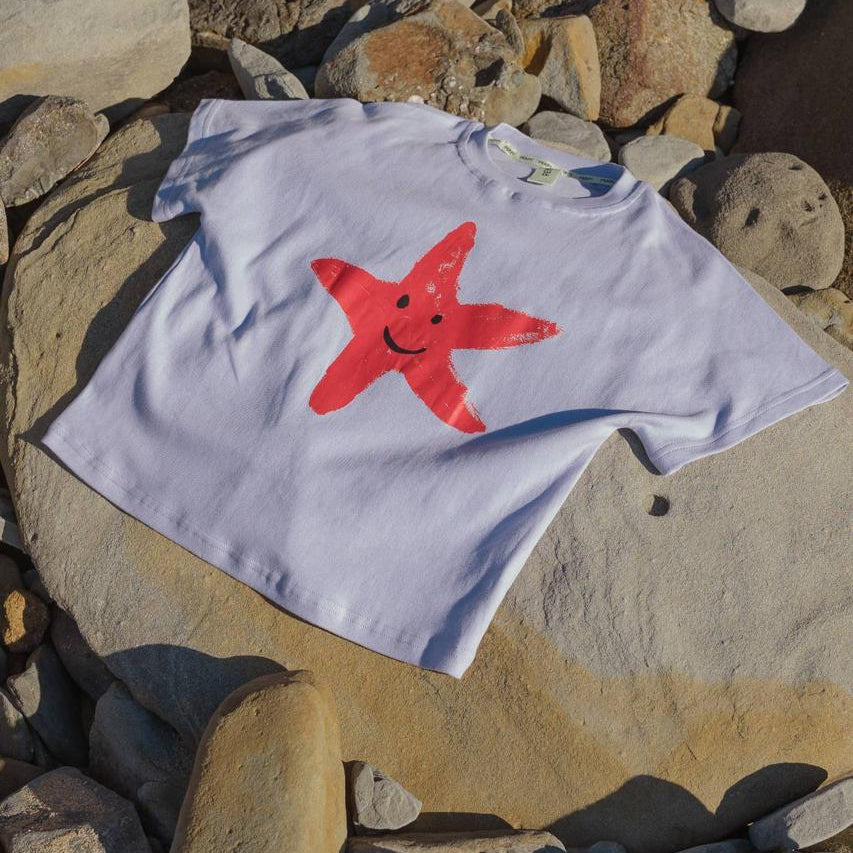 Starfish Tee Crop Purple - flat lay on beach rocks