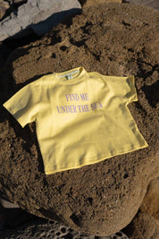 Sea Tee Crop Yellow - flat lay on beach rocks