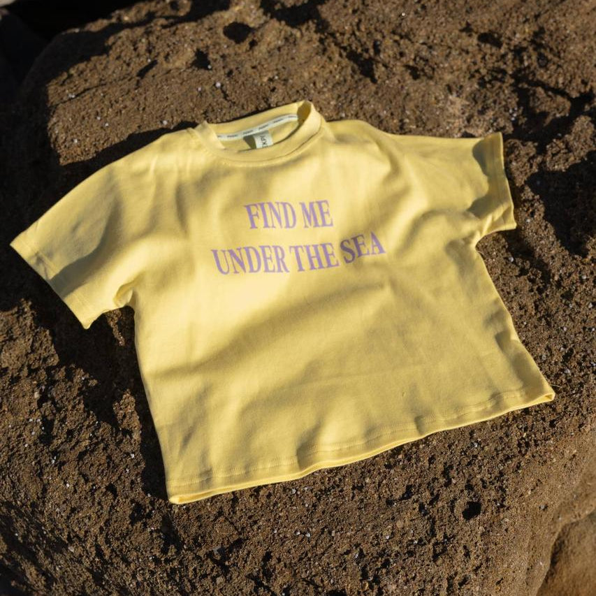 Sea Tee Crop Yellow - flat lay on beach rocks