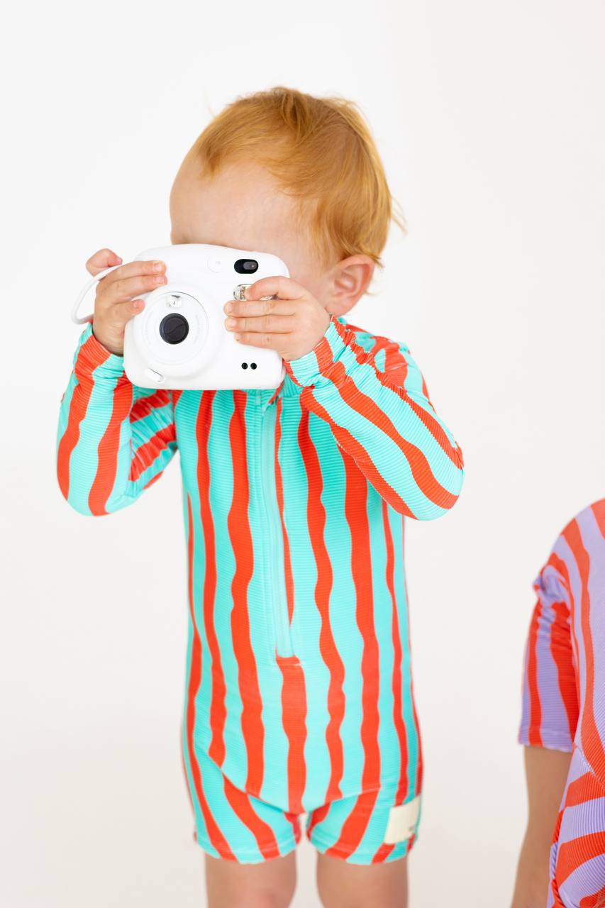 Toddler with Polaroid camera wearing Sea Kelp Aqua Shortie