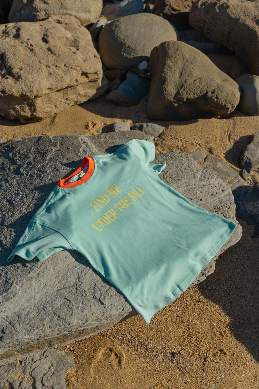 Sea Tee Green - flat lay on beach rocks