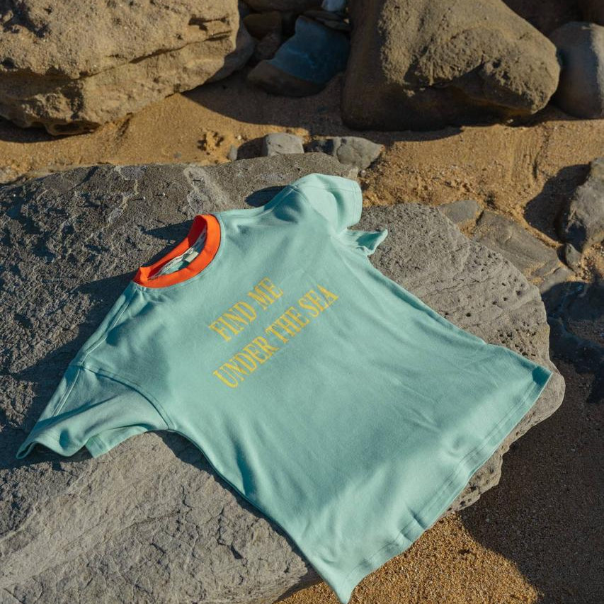 Sea Tee Green - flat lay on beach rocks