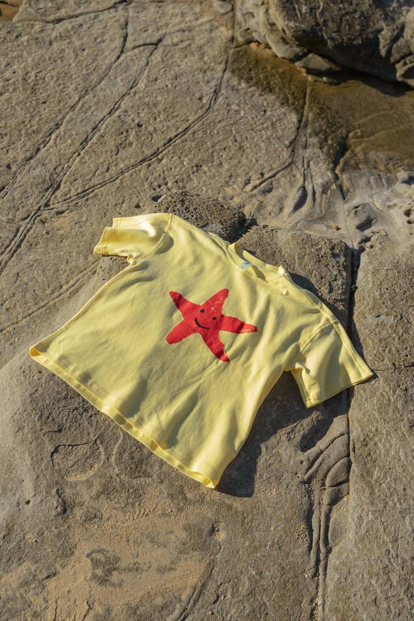 Starfish Tee Yellow - flat lay on beach rocks