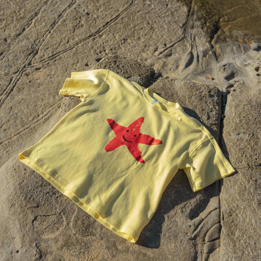 Starfish Tee Yellow - flat lay on beach rocks