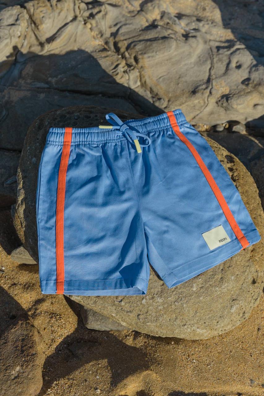 Blue Reef Shorts - flat lay on beach rocks with orange stripe detail