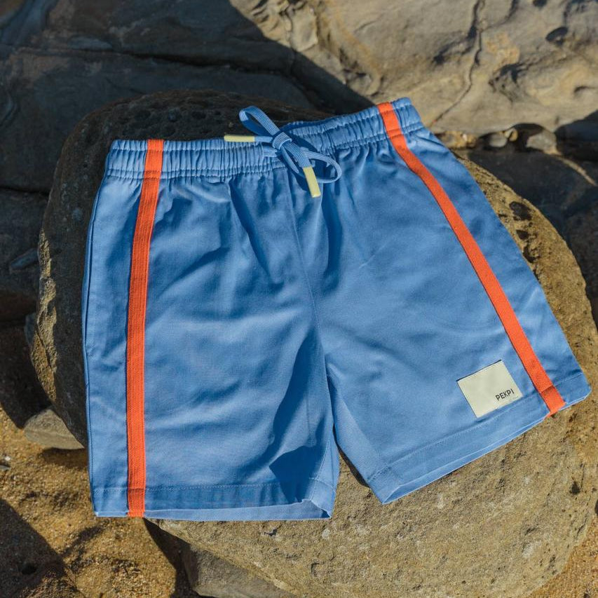 Blue Reef Shorts - flat lay on beach rocks with orange stripe detail