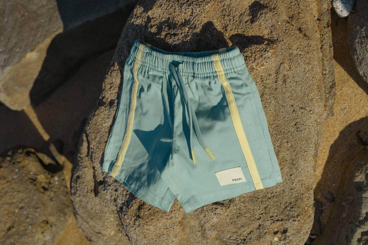 Green Reef Shorts - flat lay on beach rocks with Pekpi label