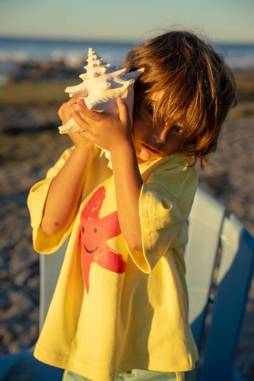 Starfish Tee Yellow - child listening to shell at beach