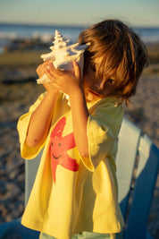 Starfish Tee Yellow - child listening to shell at beach