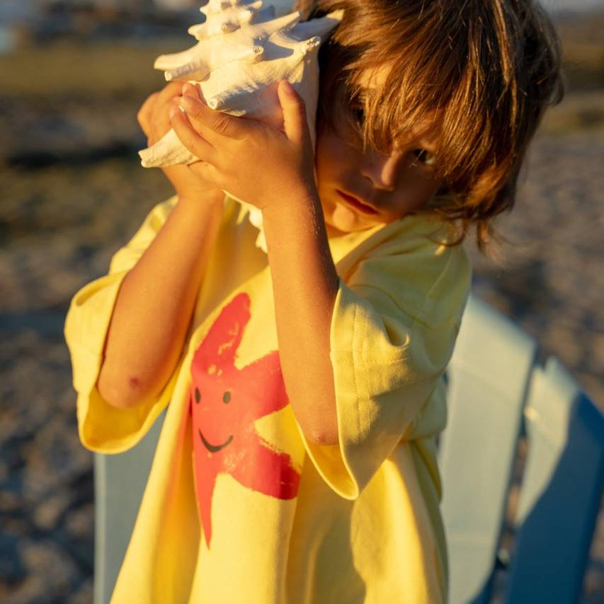 Starfish Tee Yellow - child listening to shell at beach