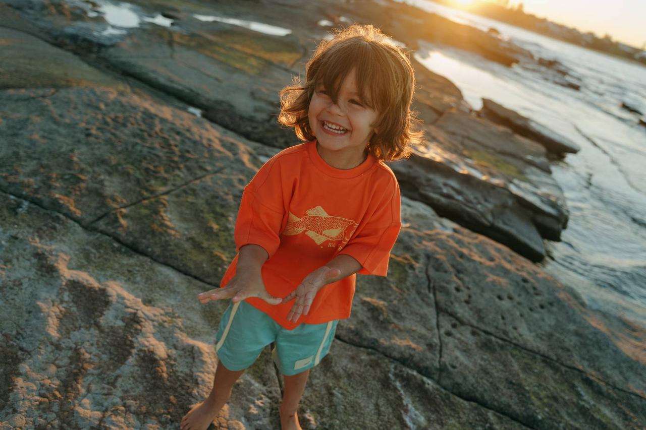 Green Reef Shorts - boy laughing on rocks with Big Glub Tee sunset